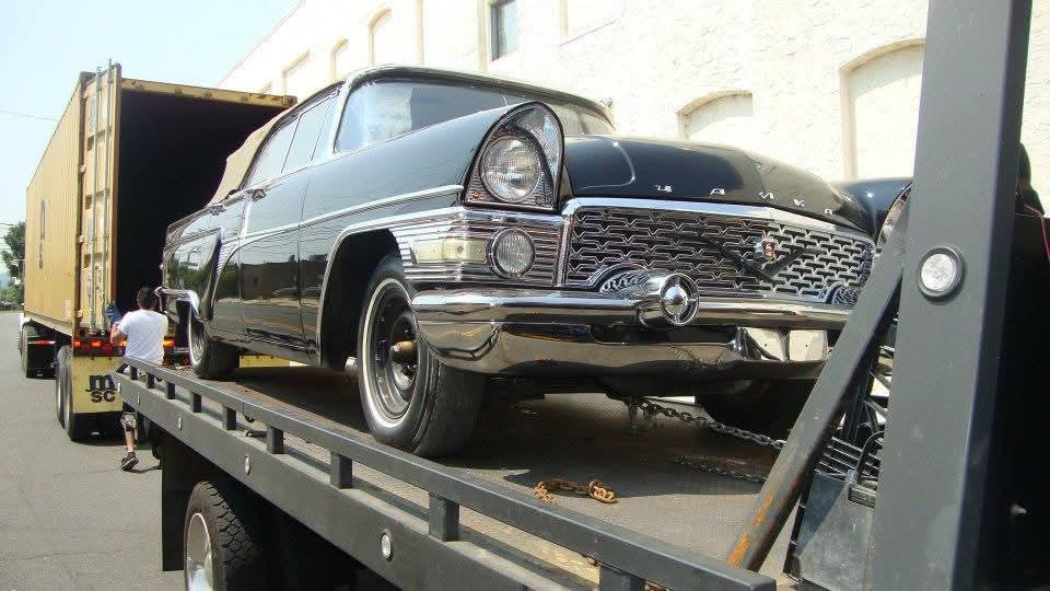 Classic car pickup by transporter beside a container truck