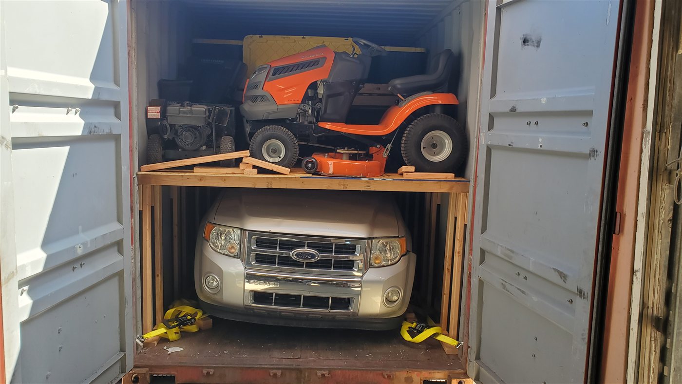 SUV secured below lawn equipment inside a shipping container