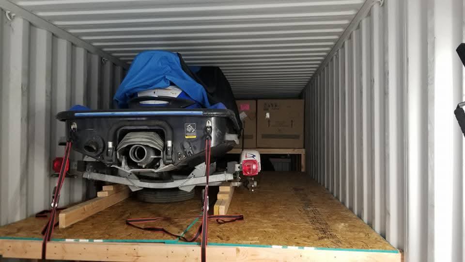 Jet ski on its trailer secured inside a shipping container with boxed cargo behind it